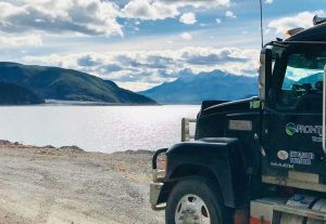 Front of a truck overlooking water and hills with blue sky and clouds
